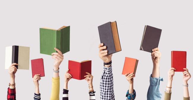 A series of arms hold up coloured, hardback books in a line against a plain background