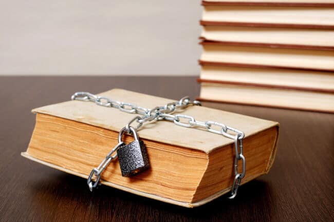 An old book is covered in chains and a padlock. In the background is another stack of books.