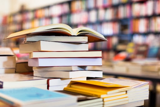 A stack of open books sit on the edge of a table in a library