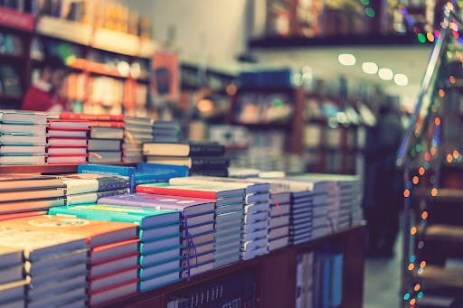 A collection of colourful books sit on a shop table with fairy lights in the background