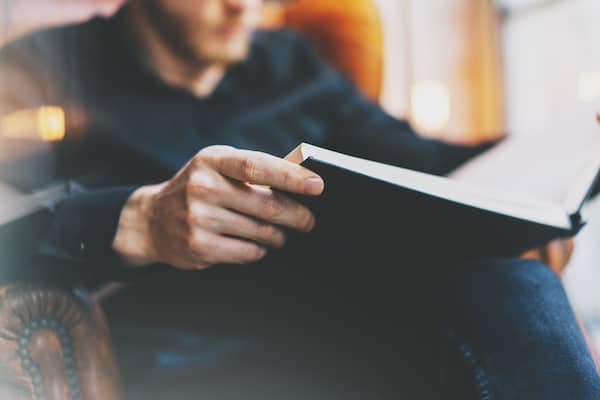 A person sits and reads a non-fiction book in an arm chair.