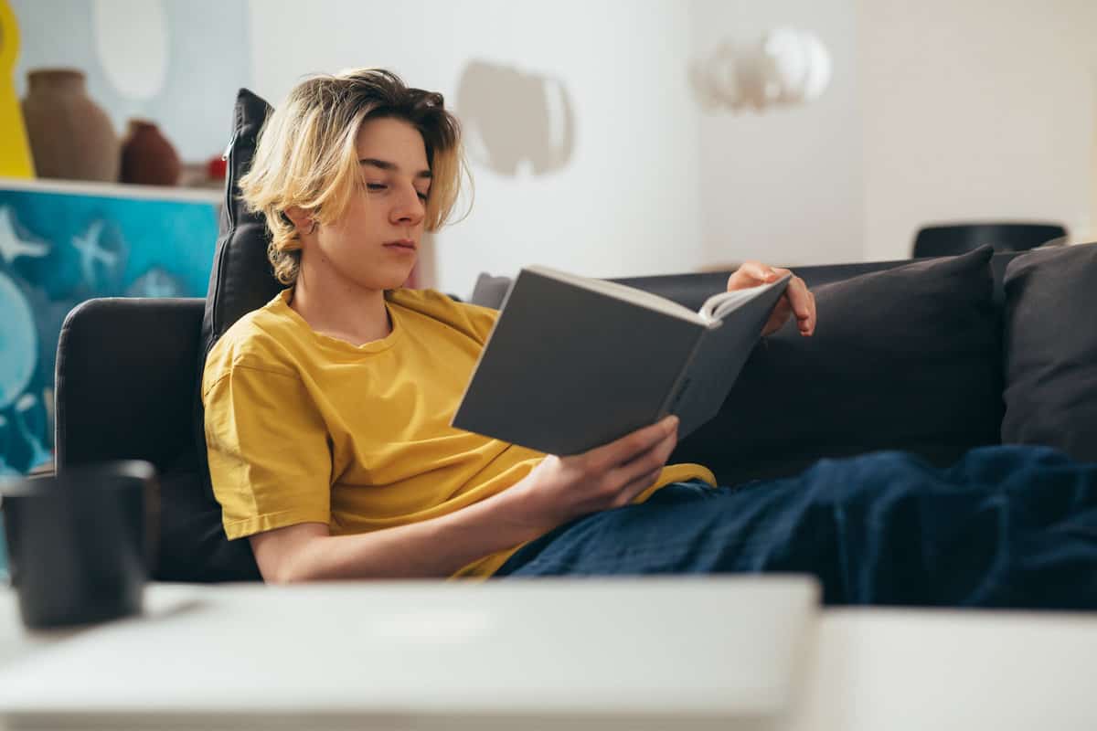 A teenager relaxes with a book on the sofa.