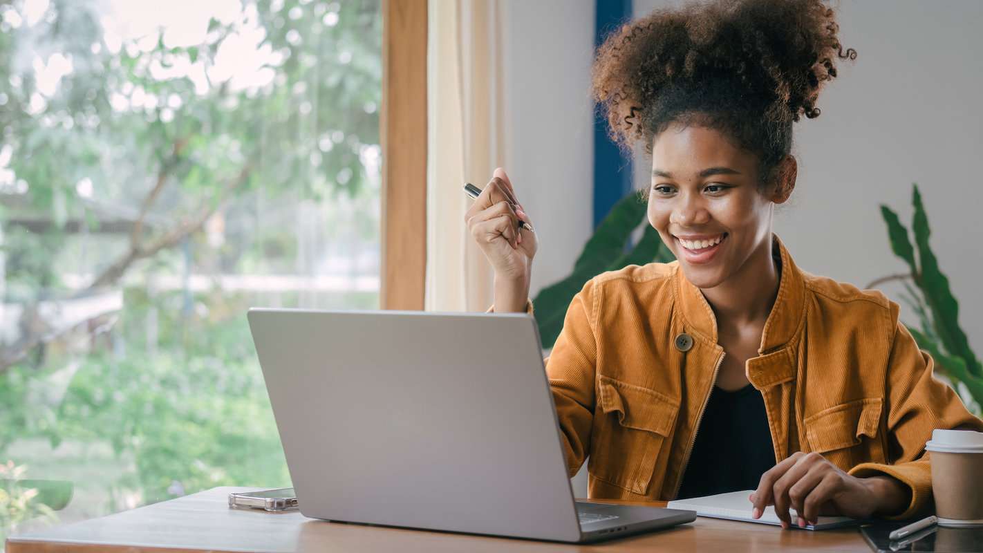 An author smiles at their laptop while holding a pen