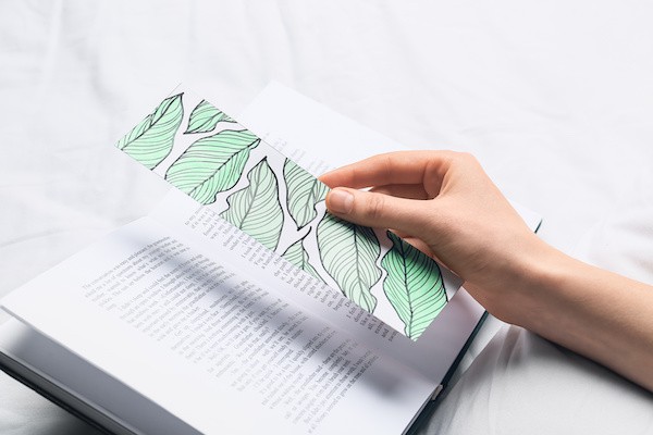 A hand places a bookmark with a leaf design into a book.