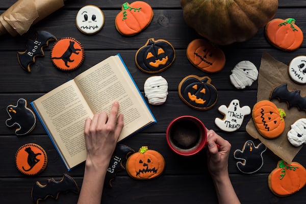 A hand points to a book surrounded by Halloween cookies and a cup of coffee.