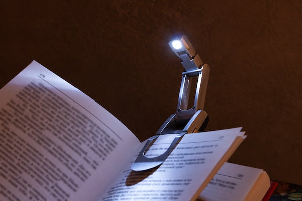 A reading light is clipped onto the pages of a book, illuminating them.