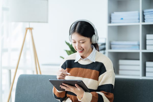 A person reads on a tablet while wearing noise canceling headphones.