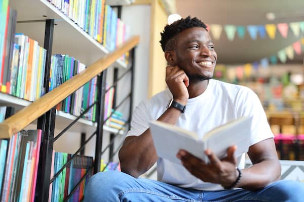 A person smiles and holds a book in a library.