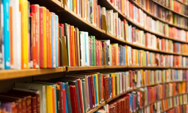 Books with different coloured spines stacked on a curved shelf.