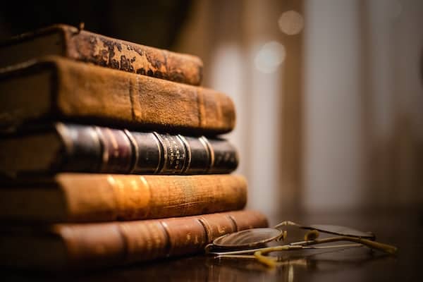 A stack of vintage books next to some wire-framed glasses.