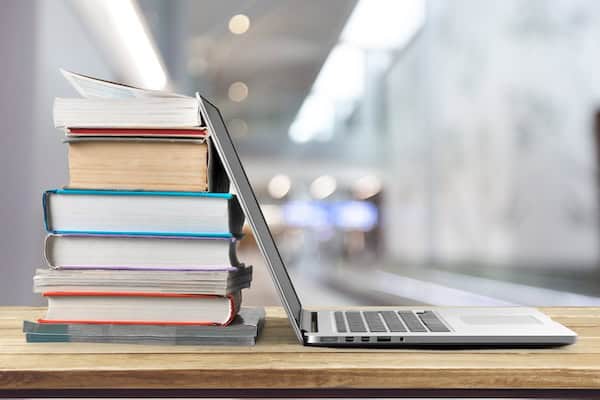 A laptop propped open on a pile of books.