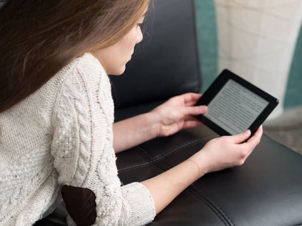 A woman reads a Kindle on a sofa.