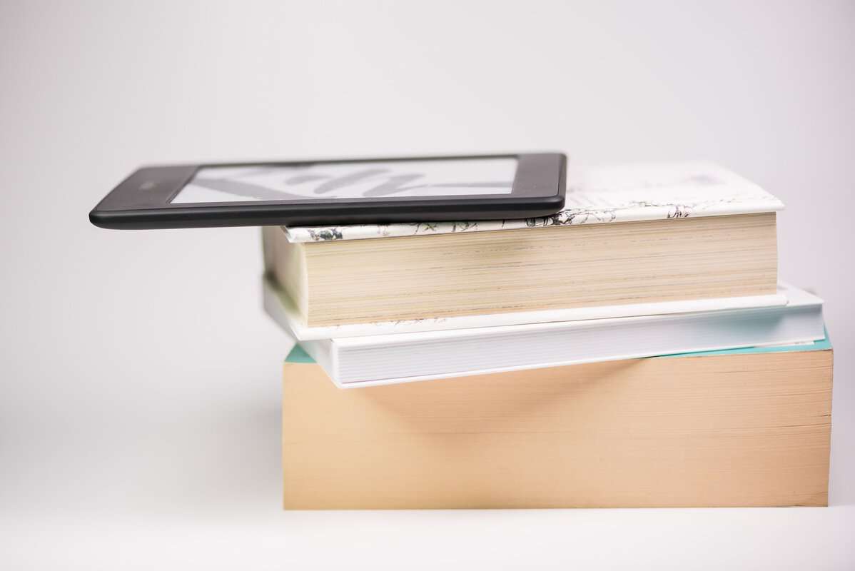 A Kindle sitting on a stack of books.