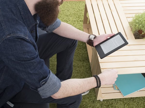 A man reading a Kindle on a bench outdoors.