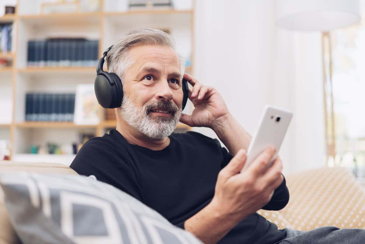 A person sits on a sofa and listens to a podcast from their smart phone.