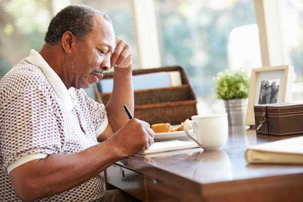 A man sat at his desk with a hot drink, writing his memoir.