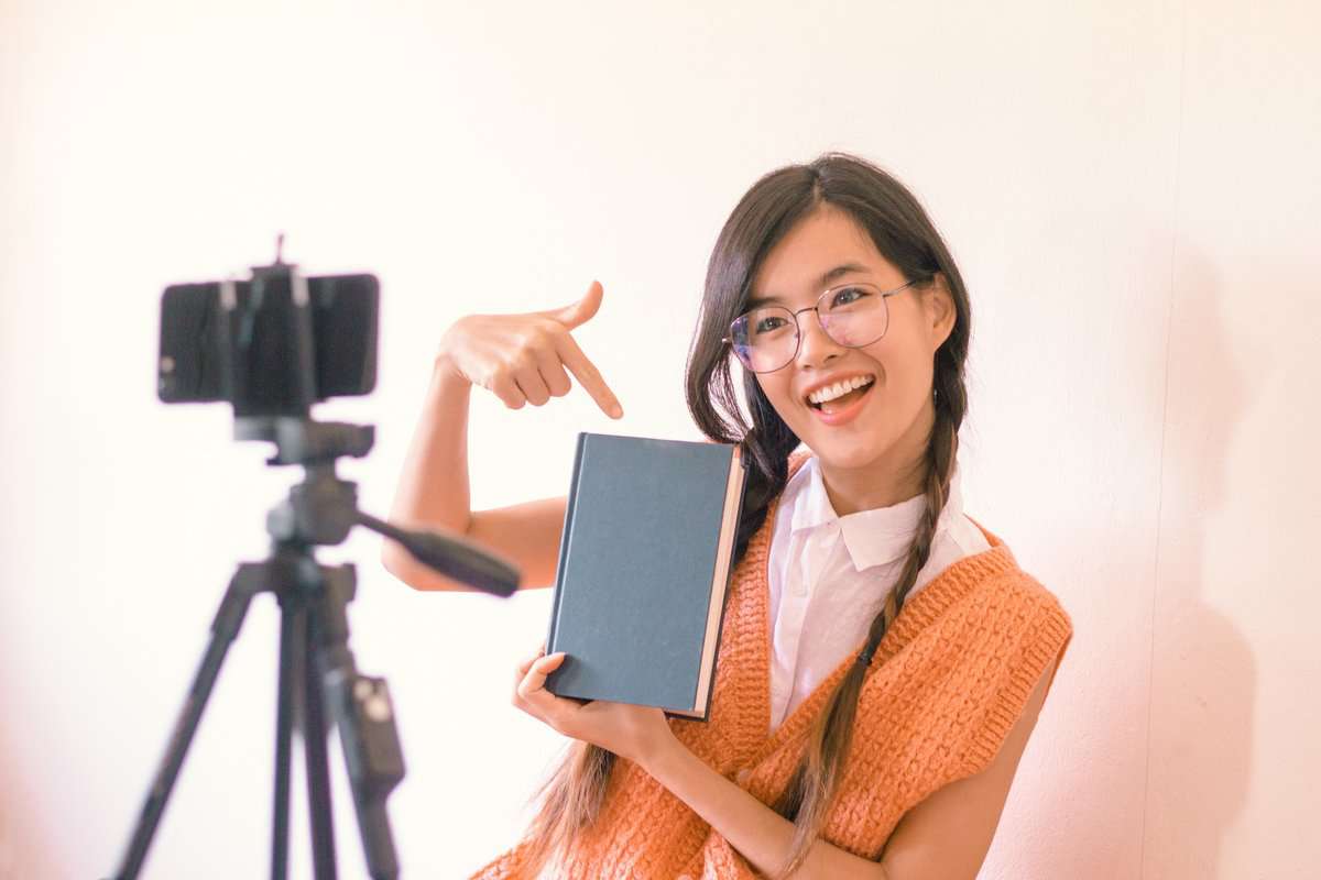 A person pointing at a book in front of a camera tripod set up.