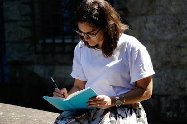 A person sitting on a wall and writing in a notebook.