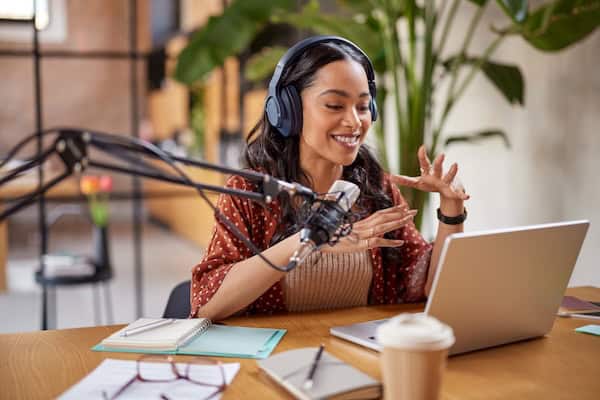 A person sitting at a desk to talk on a podcast with headphones and a microphone.