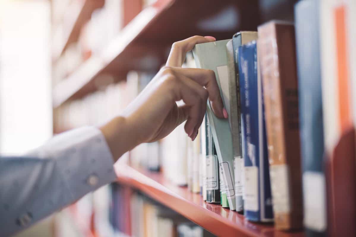 A hand selects a library book from a shelf.