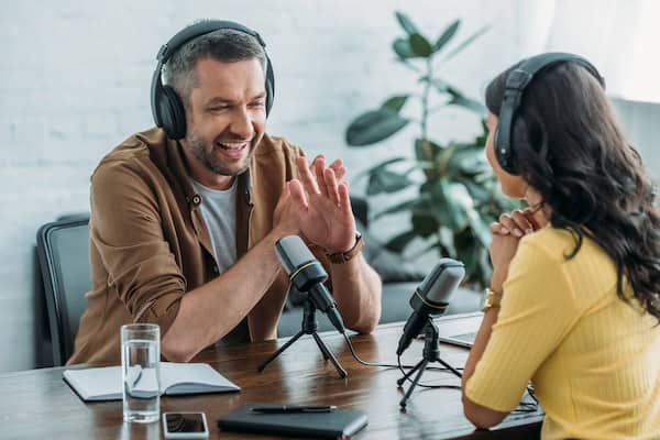 Two podcast co-hosts talk into microphones.