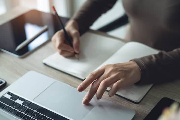 A person using a laptop and a notebook to write notes