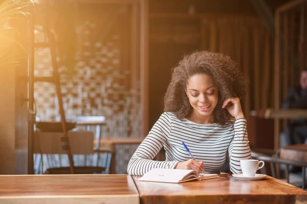 A woman writes in a notebook while sat at a table.