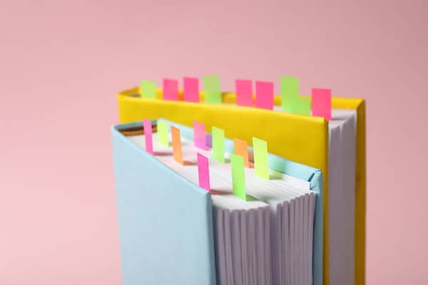 Books with colorful tabs on pink background, closeup.
