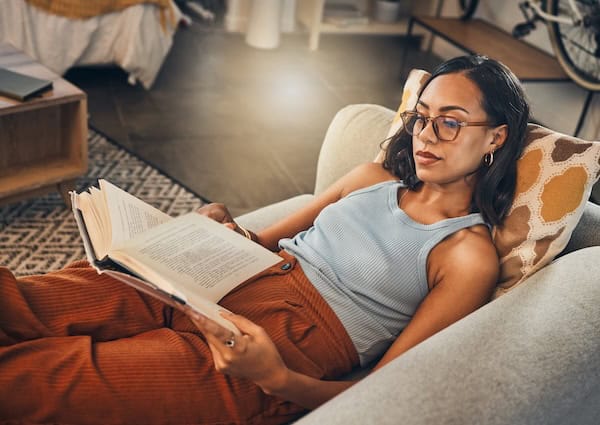 A woman stretched out on the sofa engrossed in a book.