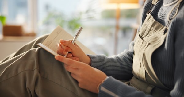 A mid shot of a woman's hands writing in her journal.
