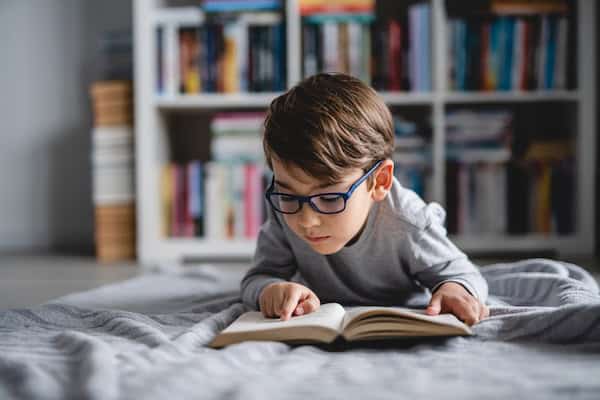 A young boy with glasses engrossed as he reads a book.