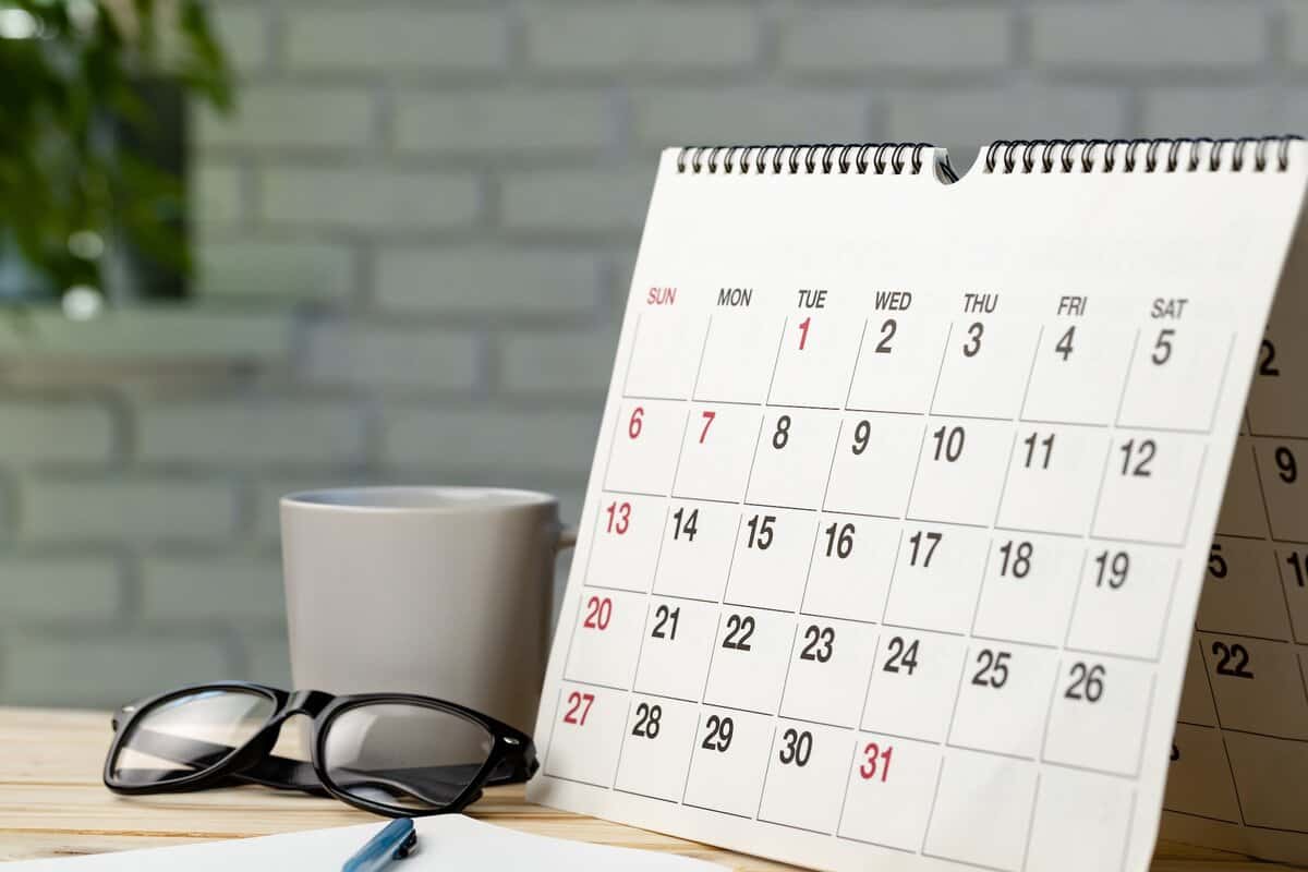 A calendar on a desk with a mug, pen, and a pair of glasses.
