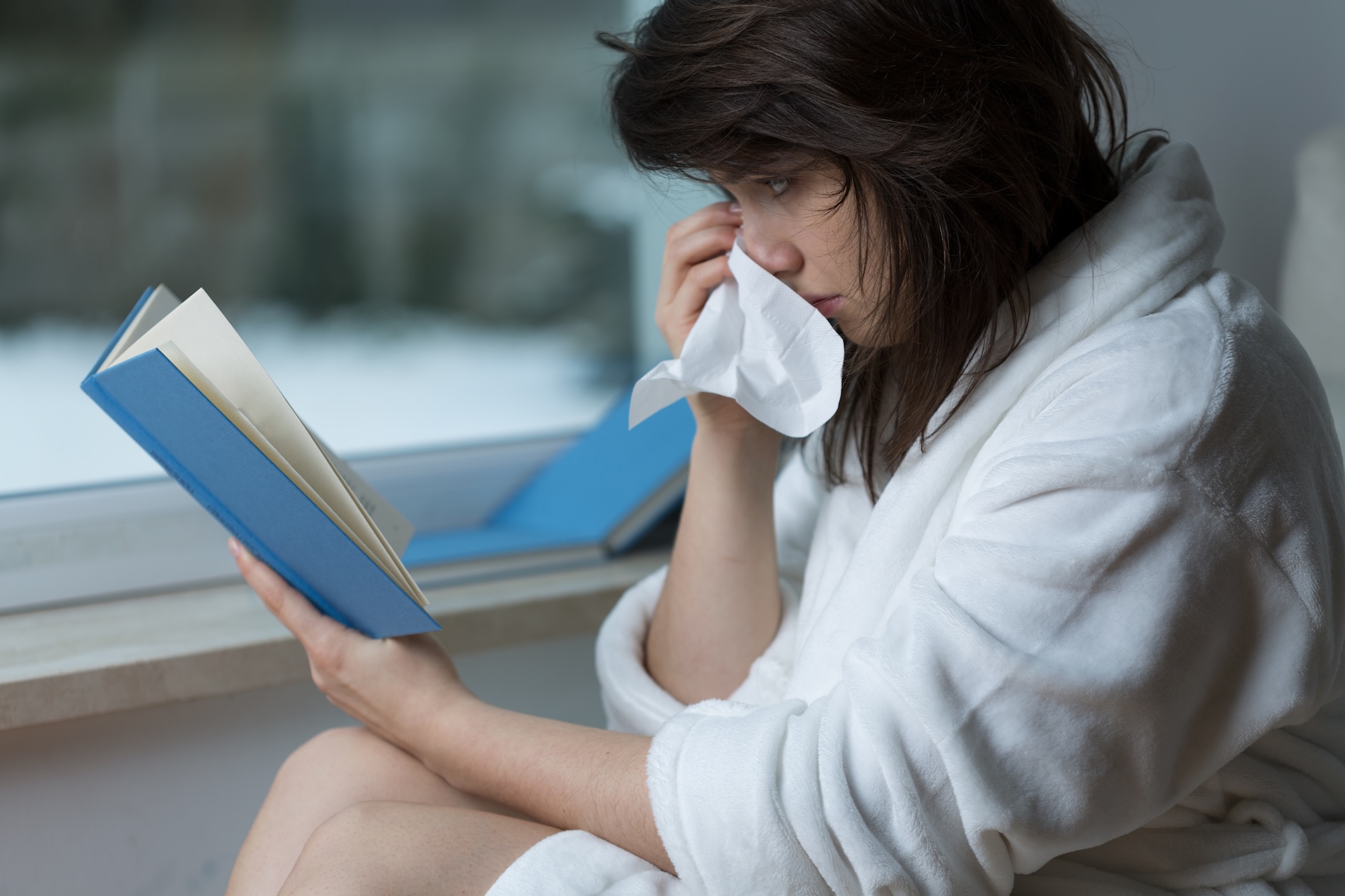 A person drying their eyes with a tissue while reading a book.
