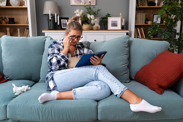 A person crying while reading a book on the sofa.