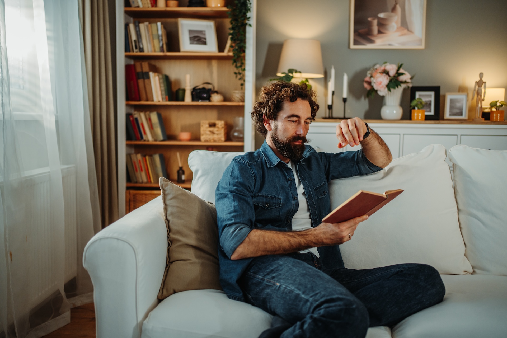 Man relaxing at home reading book on sofa enjoying some quiet time.