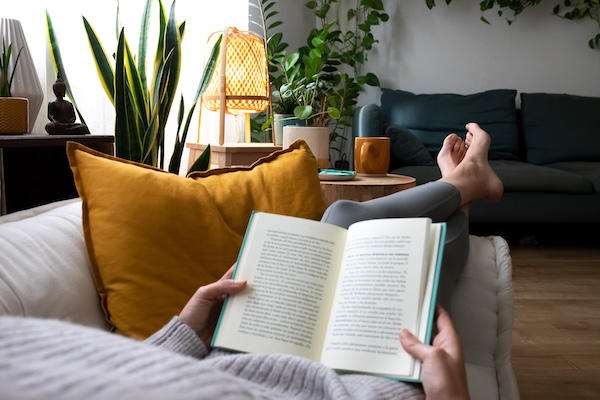POV of young woman relaxing at home reading a book lying on sofa