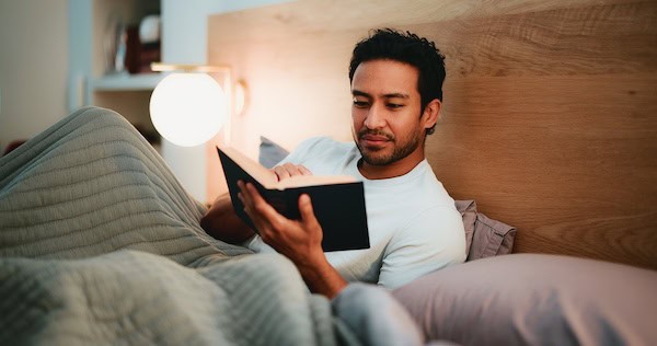 Man engrossed in a book at night as he relaxes at home in bed.