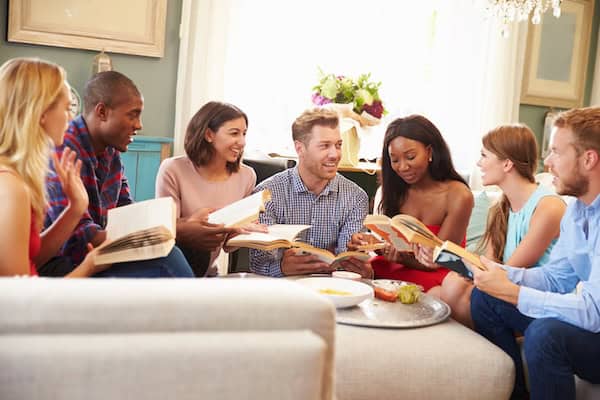 A group of friends sat around a sofa taking part In a book club at home.